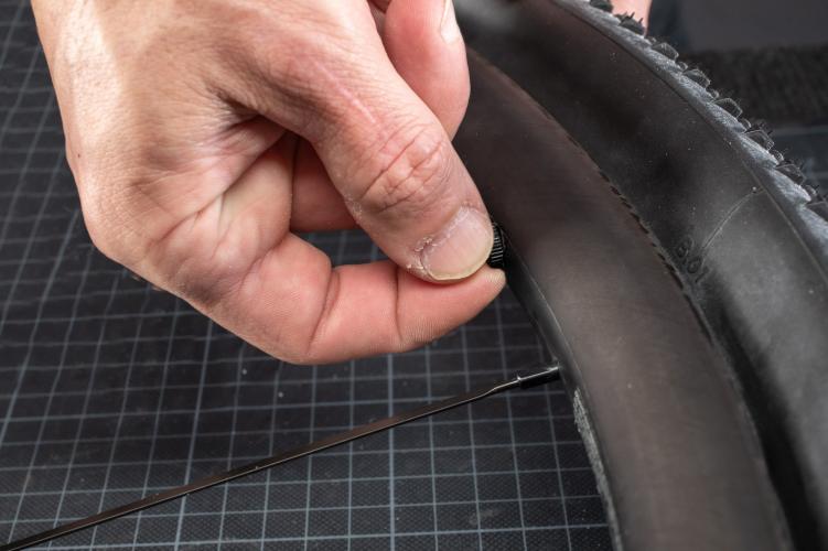 Sobald der Reifen komplett auf der Felge sitzt, drücken wird das Tubeless-Ventil von oben etwas runter und wieder hoch, um sicherzustellen, dass es nirgends hängt und gerade ausgerichtet ist. Nun drehen wir die Rändelmutter entsprechend fest, damit das Ventilloch durch die Gummidichtung des Ventils luftdicht verschlossen wird.